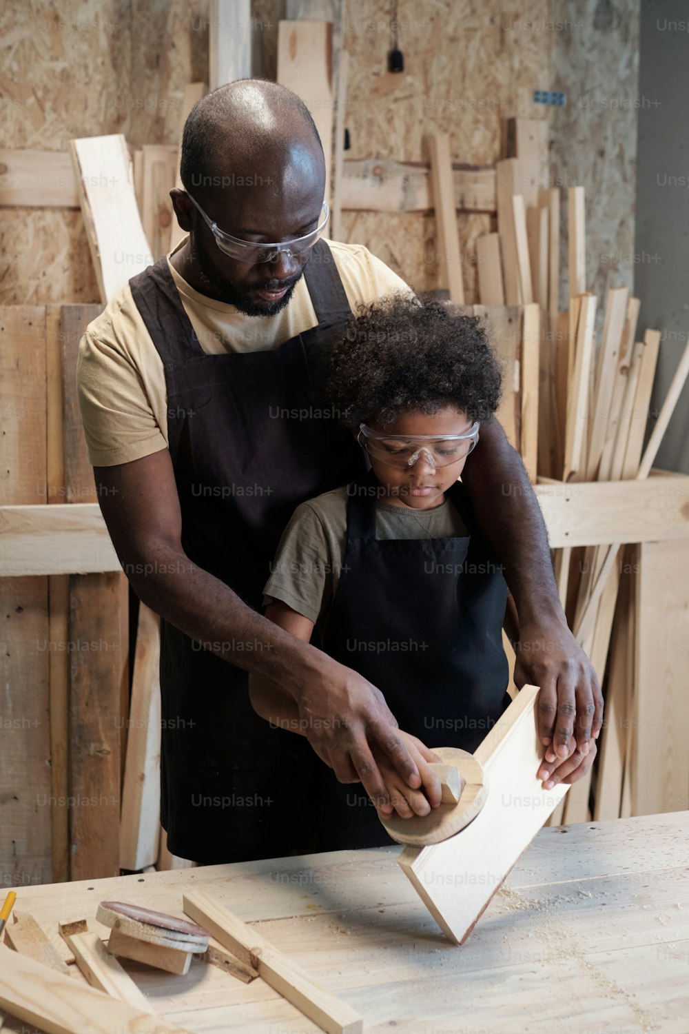 Vertikales Porträt eines fürsorglichen afroamerikanischen Vaters, der seinen Sohn in der Tischlerei unterrichtet