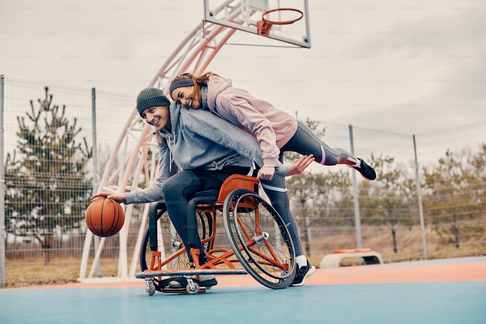 陽気な女性と車椅子の友人が屋外でバスケットボールをしながら楽しんでいる。
