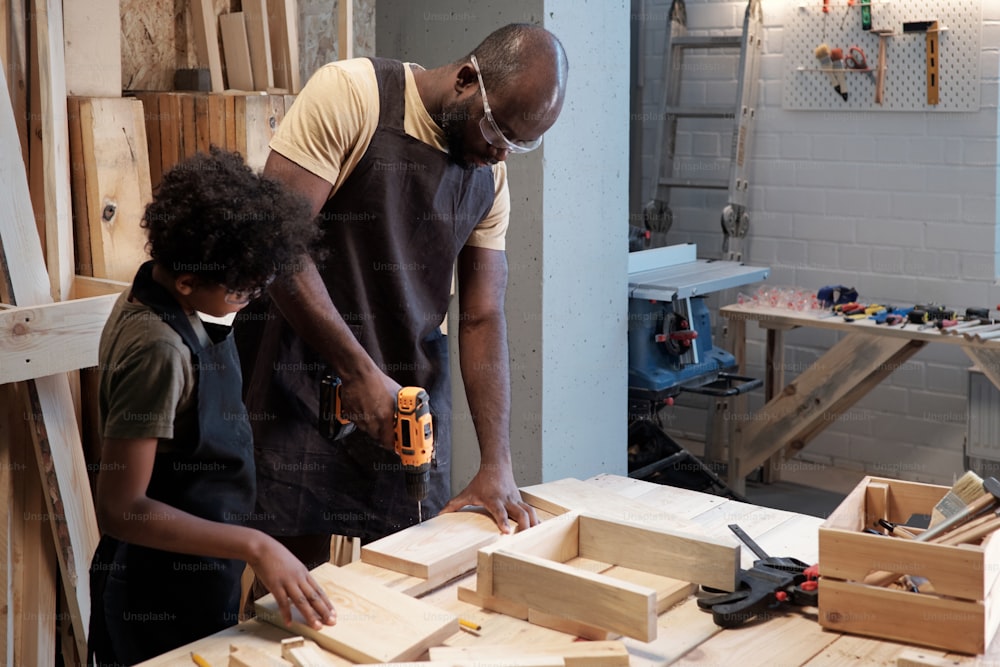 Portrait of African-American father and son building birdhouse together in garage workshop