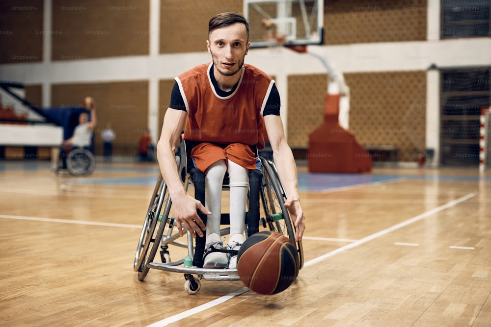 Disabled basketball player leading the ball during sports training and looking at camera.