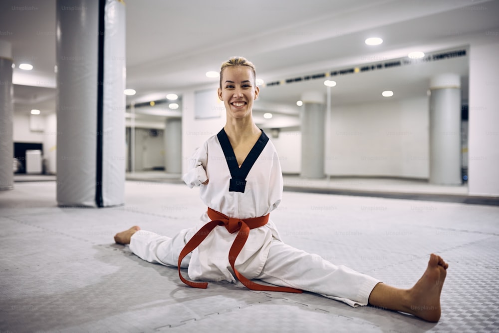 Taekwondoin feliz com uma deficiência que se estende no chão enquanto se aquece para o exercício na academia.