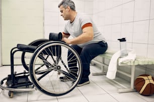 Homme athlétique handicapé ajustant son fauteuil roulant dans le vestiaire tout en se préparant pour un entraînement sportif.