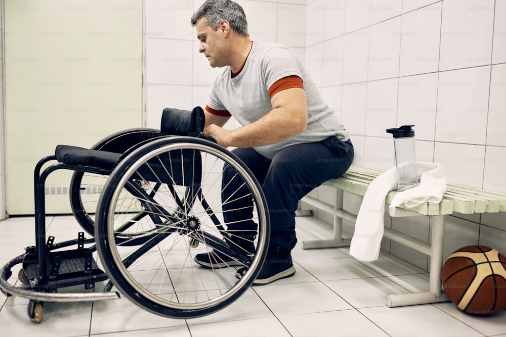 Hombre atlético discapacitado ajustando su silla de ruedas en el vestuario mientras se prepara para el entrenamiento deportivo.