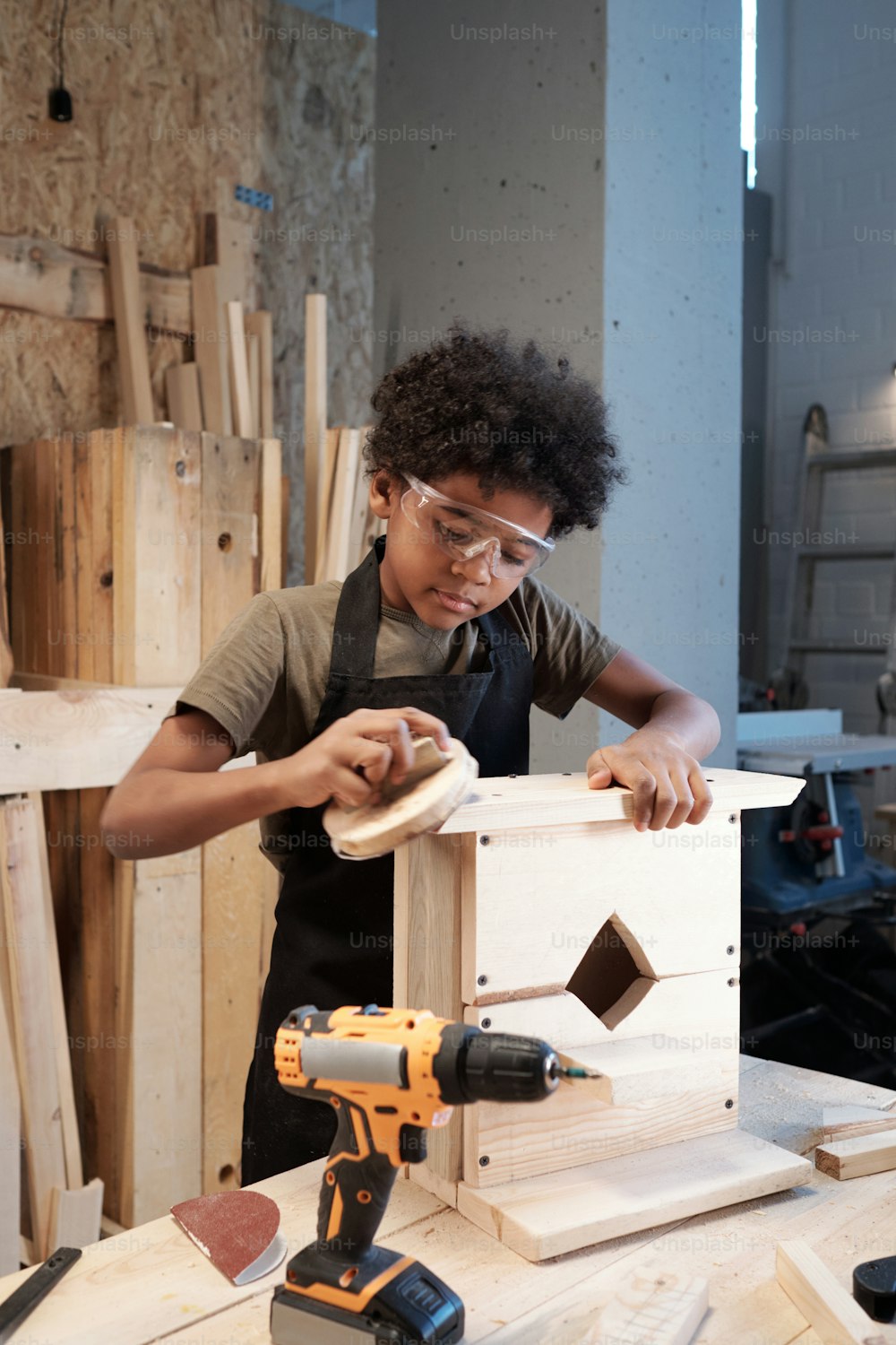 젊은 흑인 소년의 수직 초상화는 작업장에서 목조 새집을 짓고 조심스럽게 샌딩을 하고 있다