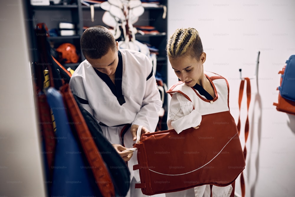 Kampfsportlerin mit Behinderung verkleiden Brustschutz mit Hilfe ihres Trainers vor dem Taekwondo-Training im Fitnessstudio.