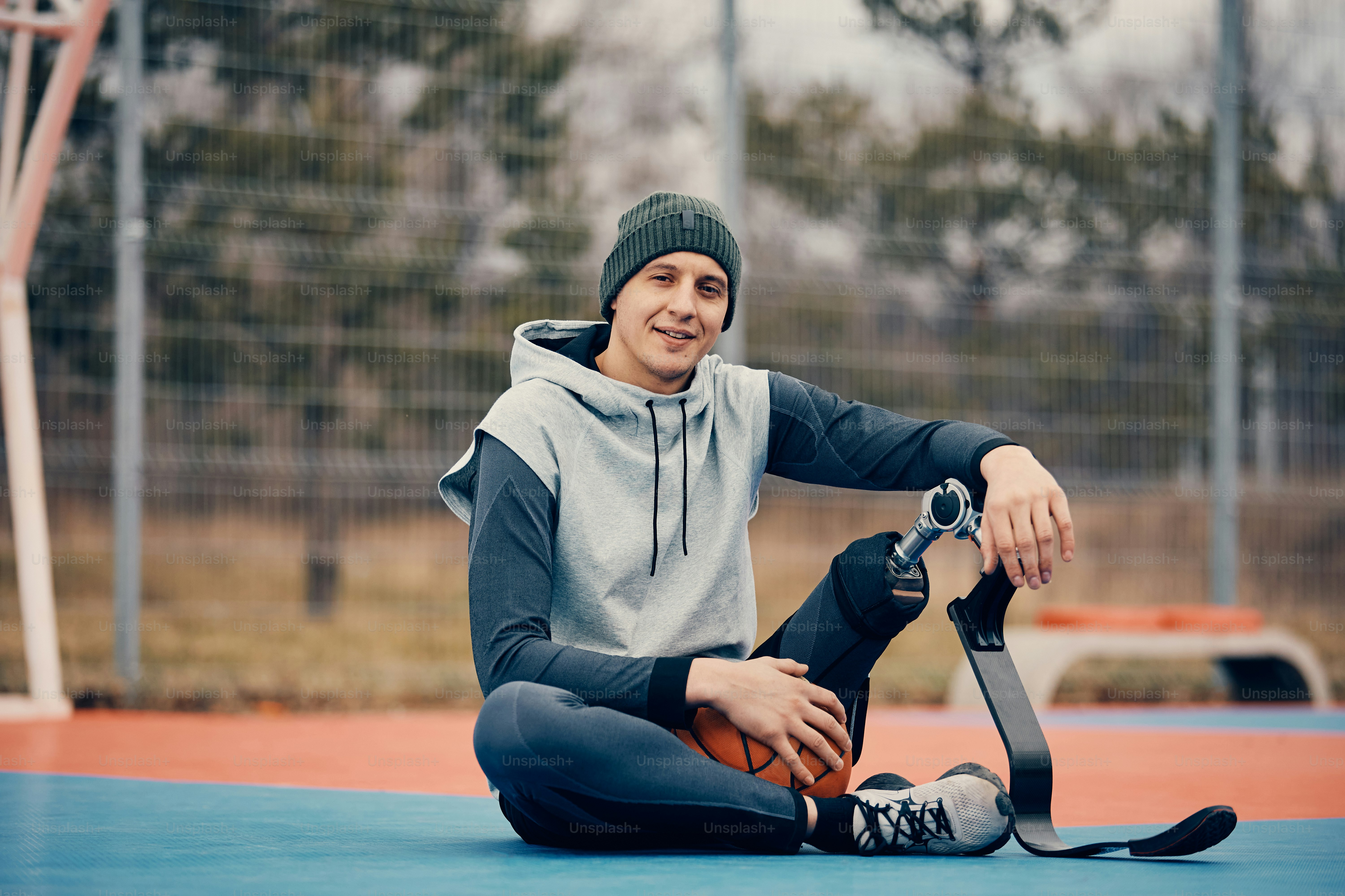 Lächelnder Basketballspieler mit künstlichem Bein entspannt sich auf dem Sportplatz und schaut in die Kamera.