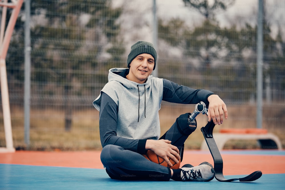 Smiling basketball player with artificial leg relaxing on sports court and looking at camera.