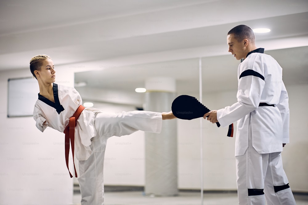 Female taekwondo fighter without the upper limbs exercising leg kick with a coach in health club.