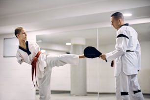 Lutadora de taekwondo sem os membros superiores exercitando chute de perna com um treinador em health club.