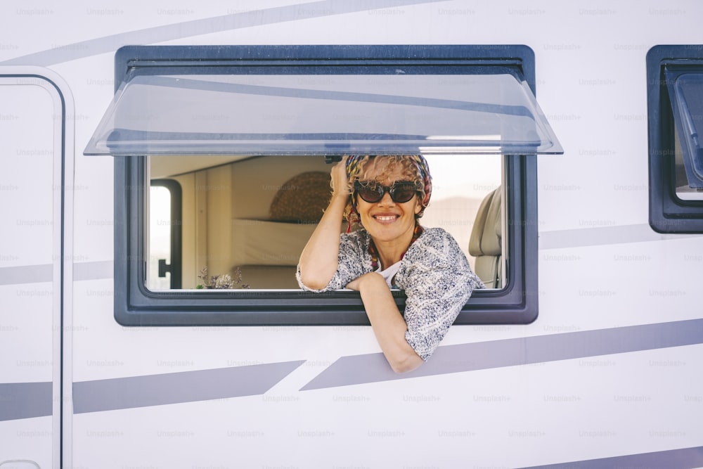 Portrait d’une femme adulte joyeuse regardant par la fenêtre d’un camping-car et appréciant le style de vie de voyage. Les femmes sourient et cherchent une photo. Vacances d’été vacances road trip touriste