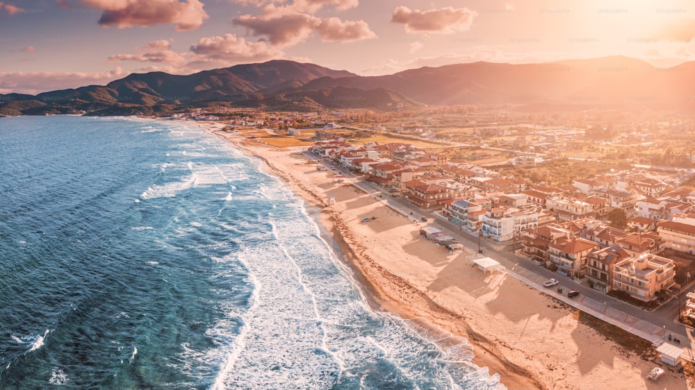 Dramatic panoramic aerial view of iconic Sarti resort town and famous long and empty sandy beach at sunset time with high waves and sun flare