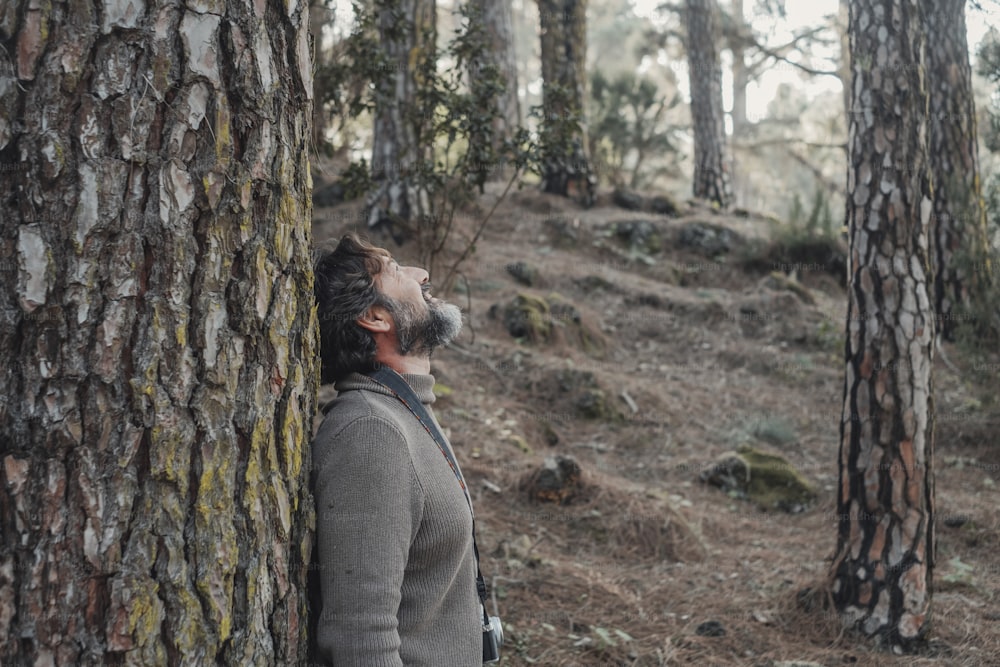 Standing man enjoying happiness and joyful feeling the outdoors nature park against a pine tree trunk. People and forest woods leisure activity. Tourist and mountains concept vholiday vacation