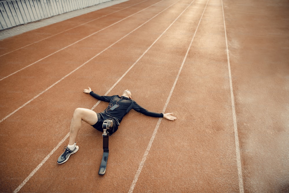 Un deportista en forma con una pierna protésica tumbado en la pista de atletismo y relajándose con la música.