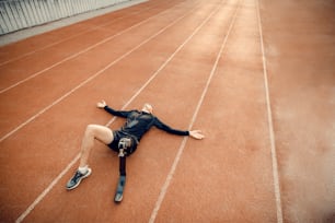 A fit sportsman with prosthetic leg lying on running track and relaxing with music.