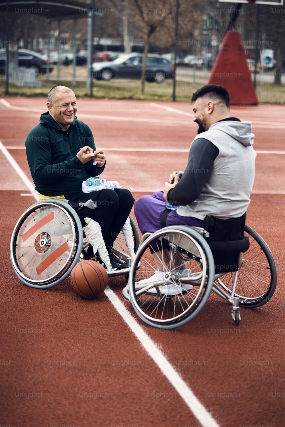 Fröhliche Basketballspieler im Rollstuhl haben Spaß bei der Vorbereitung auf das Training auf einem Outdoor-Sportplatz.