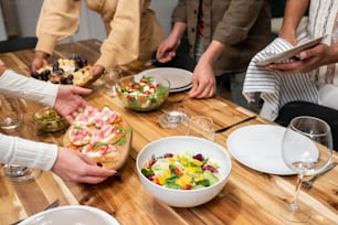 Close-up of young people putting appetizers and salad on dining table preparing for dinner party at home