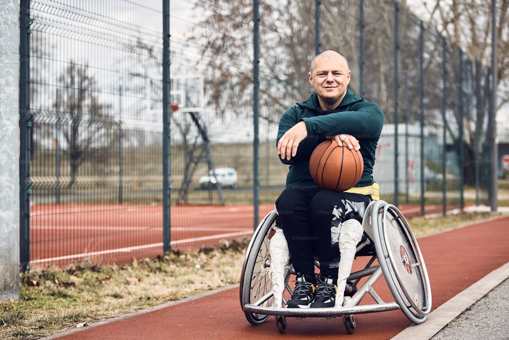 Atleta masculino sorridente com deficiência segurando basquete ao ar livre e olhando para a câmera.