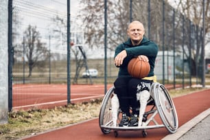 Athlète masculin souriant avec un handicap tenant le basket-ball à l’extérieur et regardant la caméra.