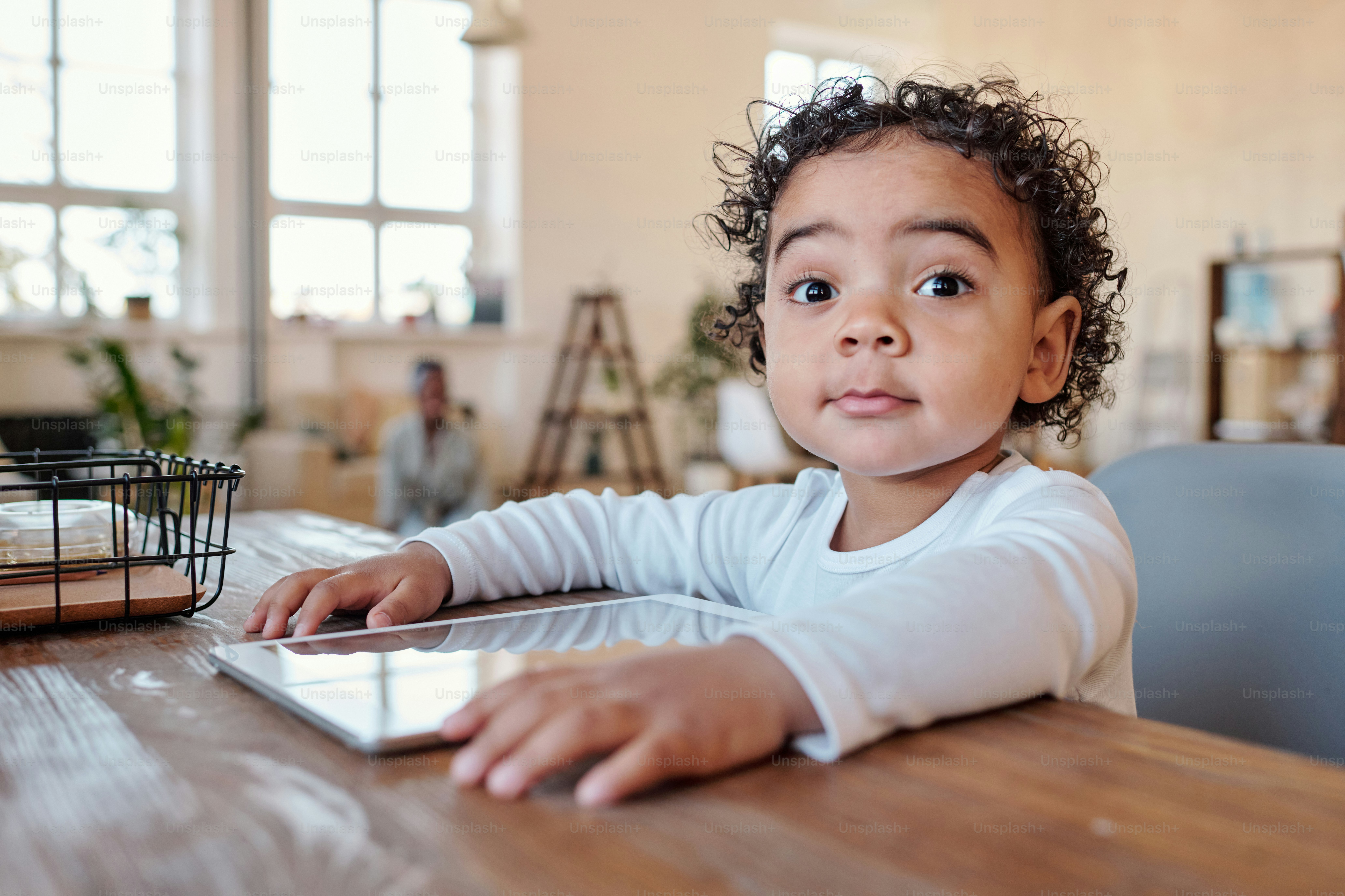 Portrait of surprised curious African-American boy with curly hair sitting at table with gadget