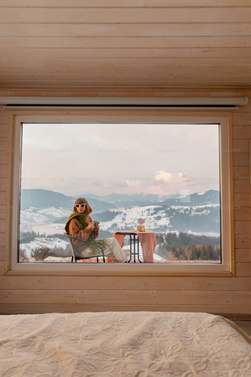 Frau sitzt mit einem Drink auf der Terrasse des winzigen Hauses in den Bergen, Blick durch das Fenster von innen. Konzept der kleinen modernen Kabinen für Ruhe und Flucht in die Natur