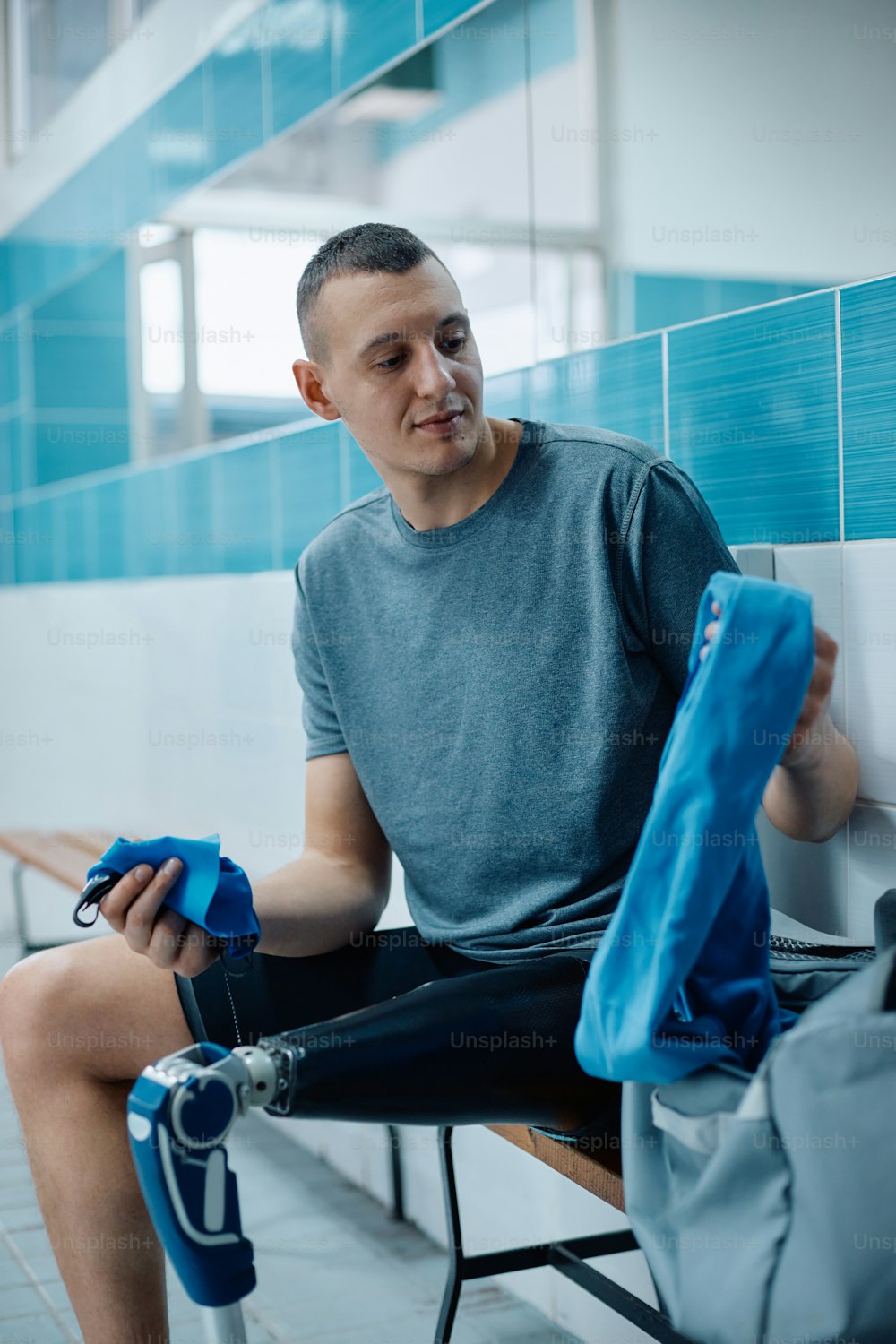 Young athlete with a leg prosthetic getting ready for swimming training in dressing room.