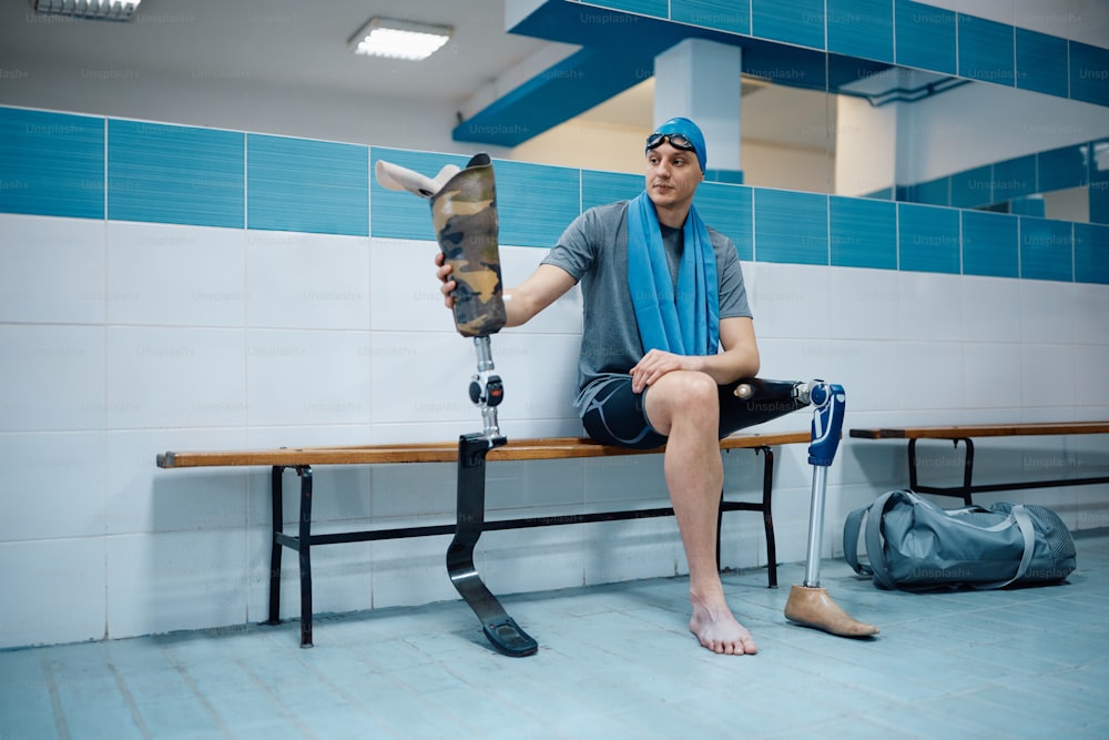 Young amputee changes his prosthetic leg while preparing for swimming training in dressing room.