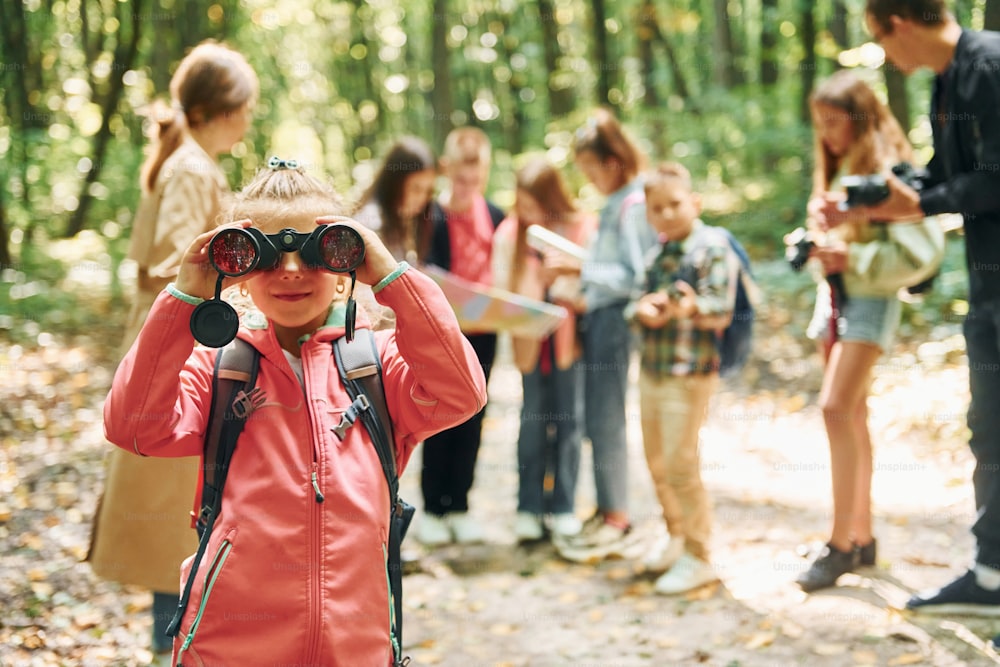 Muchacha mirando a través de binoculares. Niños en el bosque verde durante el día de verano juntos.