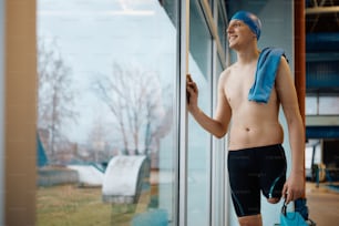 Young happy adaptive swimmer looking through the window after the practice at indoor pool. Copy space.