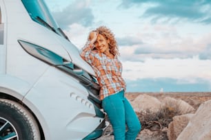 Happy adult woman tourist against modern camper van motorhome smile and look at the camera. Female people traveler enjoy destination and vacation. Country side and blue sky in background