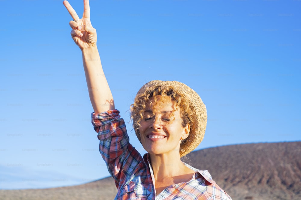 Victory hand gesture to stop war and love peace for people concept image with happy adult woman in the country side, smiling and enjoying the day. Environment and good future for earth supporter
