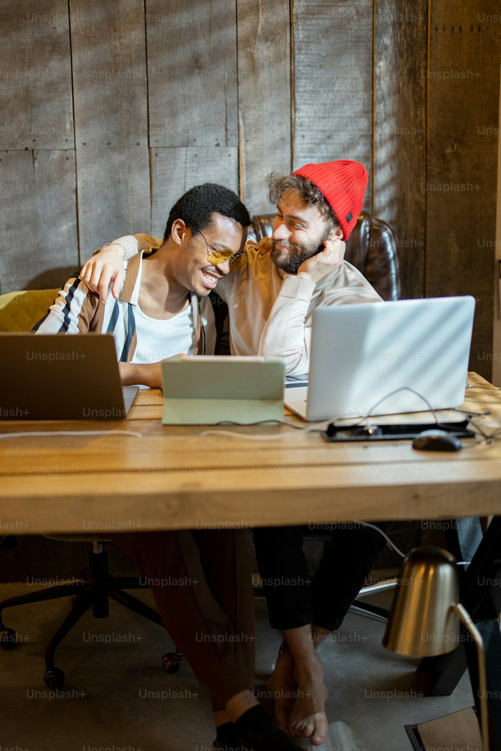 Dos hombres de diferente nacionalidad divirtiéndose mientras trabajan en computadoras en la oficina en casa. Concepto de parejas homosexuales que trabajan juntas. Hombre caucásico e hispano juntos