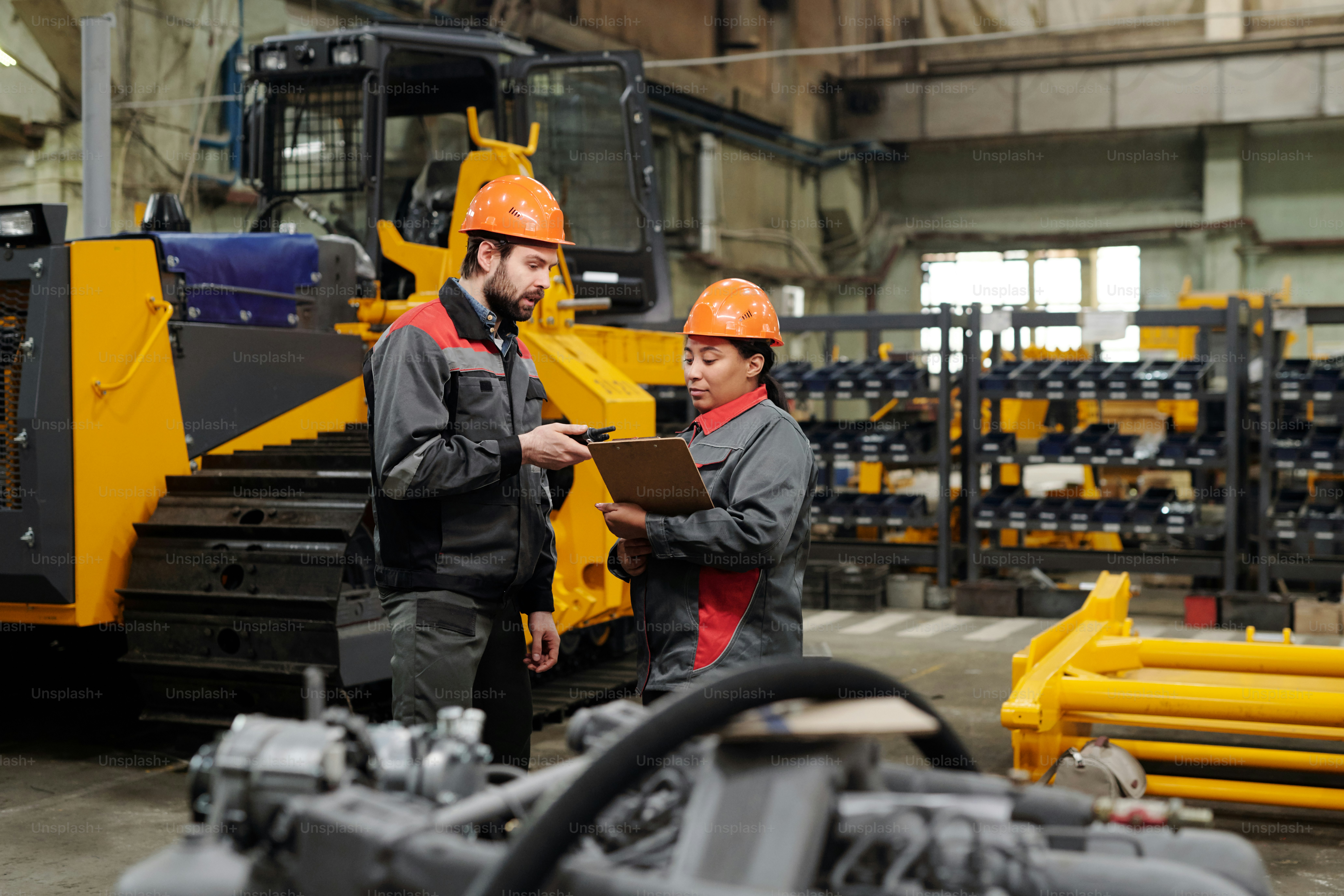 Two young workers of industrial plant in workwear discussing technical ...