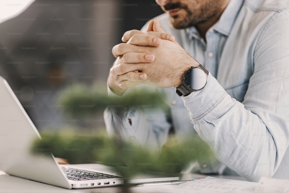 Close up of businessman looking at laptop with intertwined fingers at home.