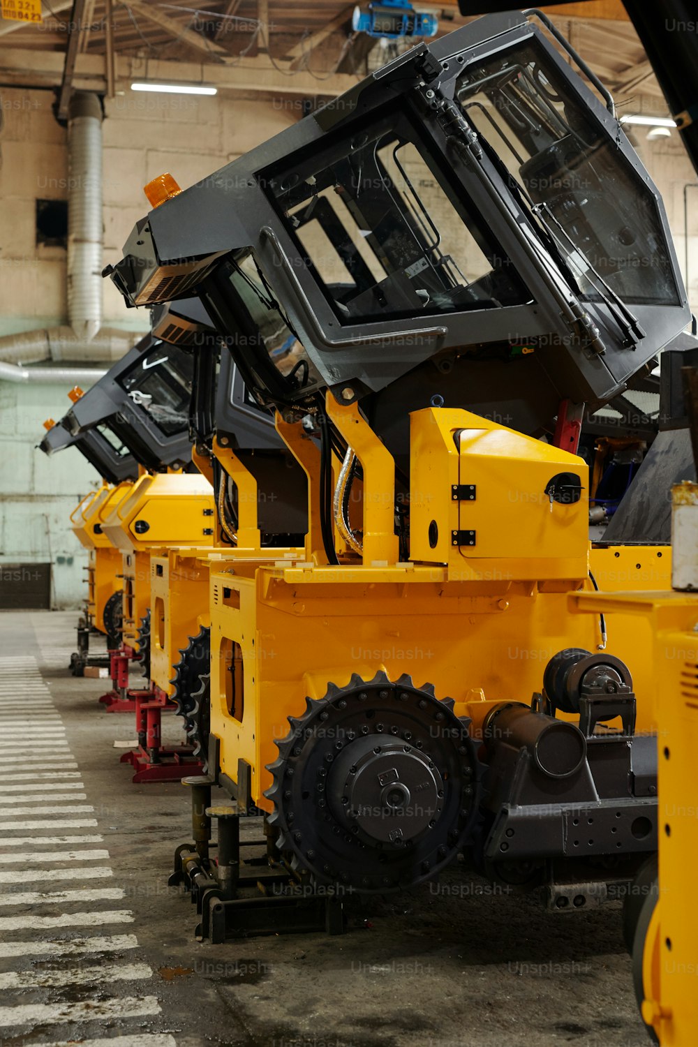 Várias máquinas de construção enormes de cor amarela em pé na fila no piso de concreto do porão, armazém ou oficina