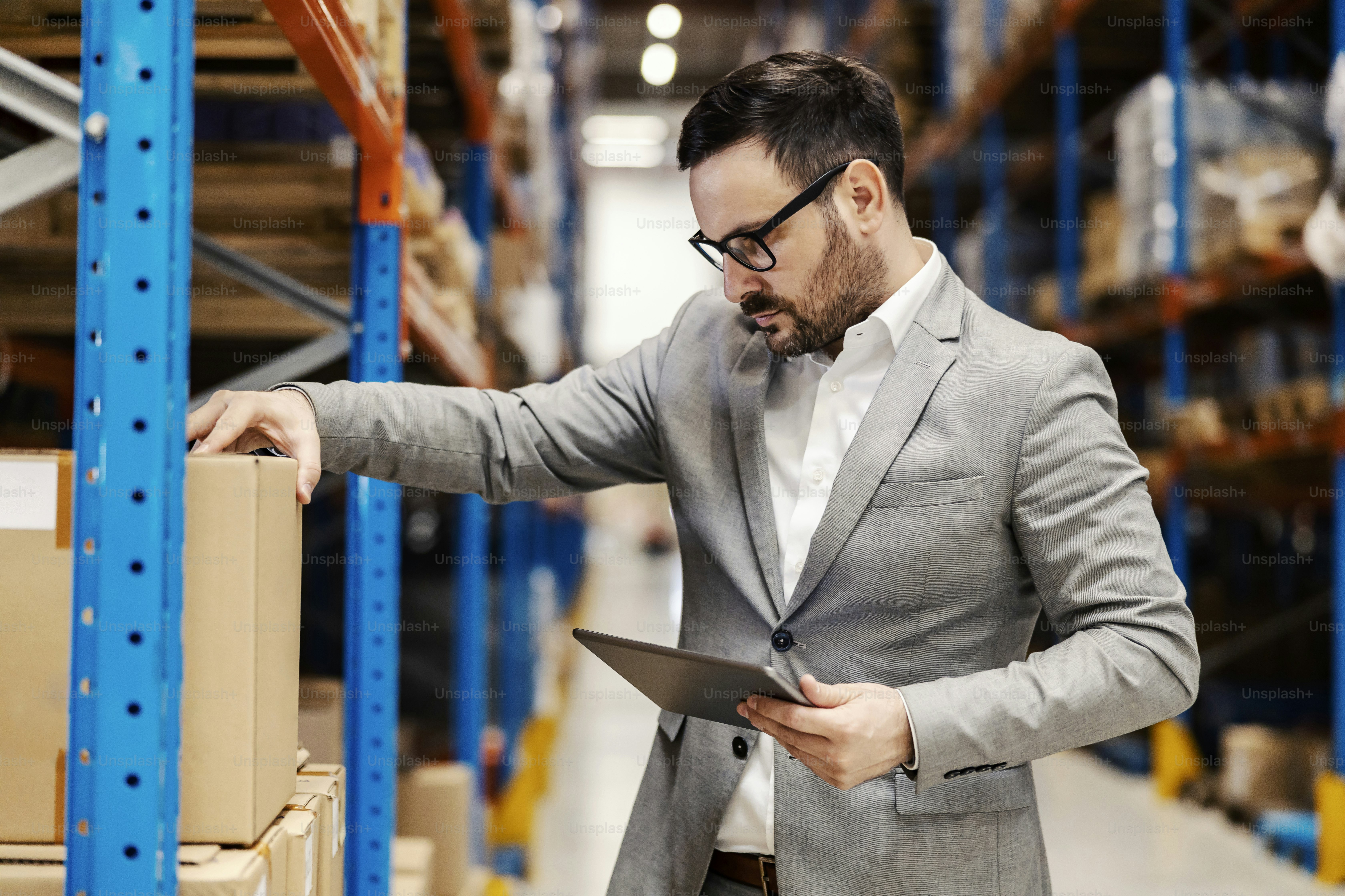 An inspector looking at box in storage and checking on order on tablet at storage.