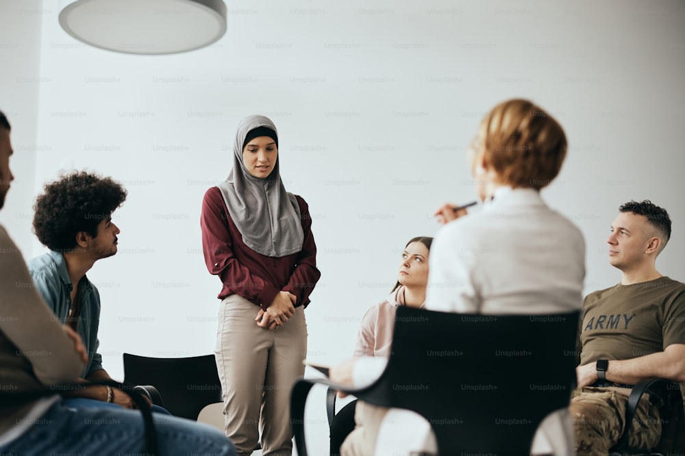 Young Middle Eastern woman introducing herself to group therapy members during a meeting at mental health center.