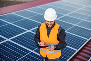 Ein Handwerker, der ein Tablet hält, um Sonnenkollektoren zu überprüfen, und lächelt das Tablet an.