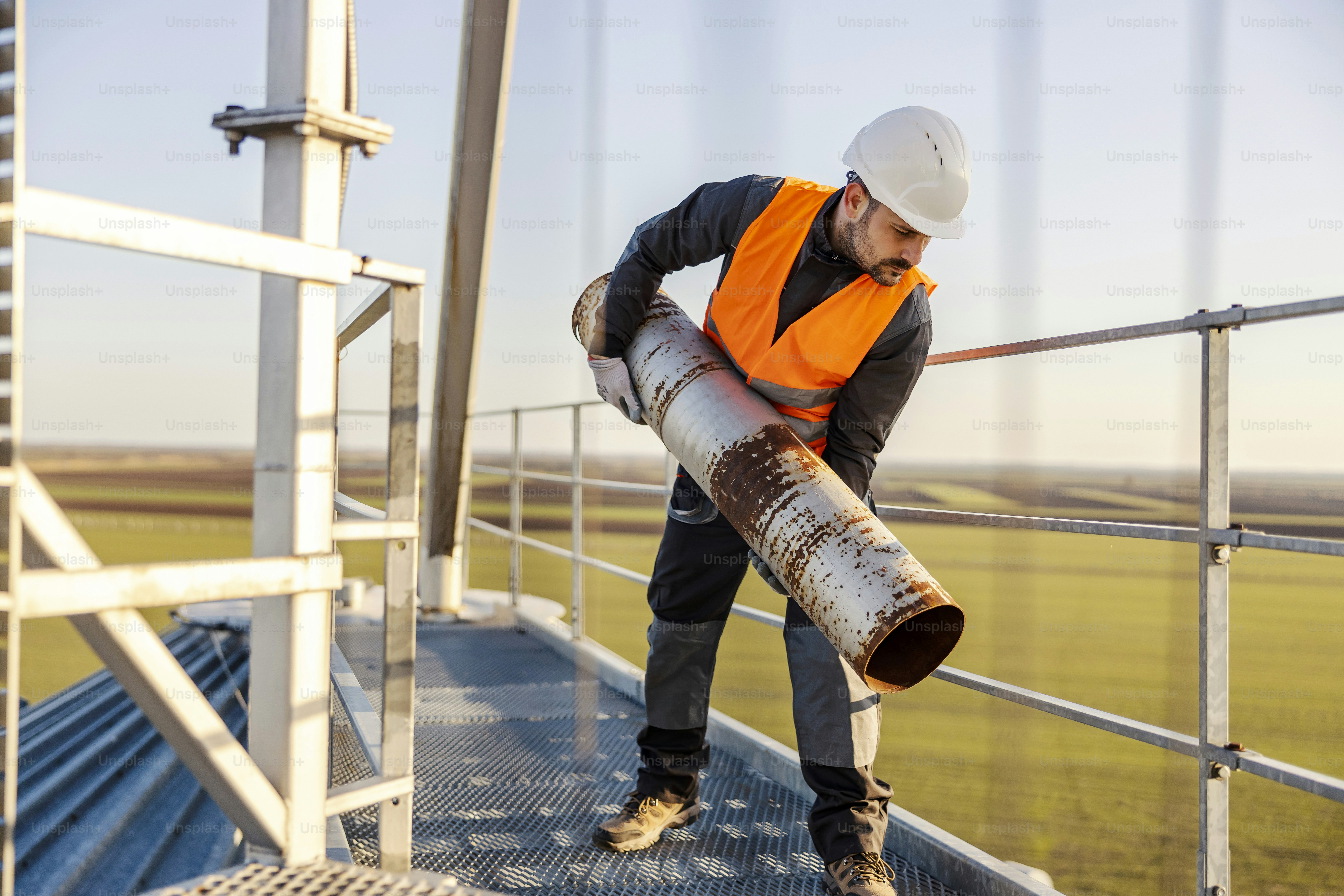 An industry worker relocating heavy metal pipe on height.