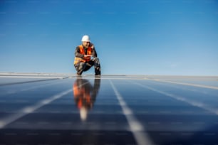 A worker speaking to the manager on the phone while crouching on the roof surrounded by solar panels.
