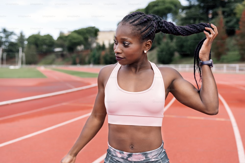 Stock photo of an African-American sprinter standing on an athletics track touching her braided hair with her hand. Sports