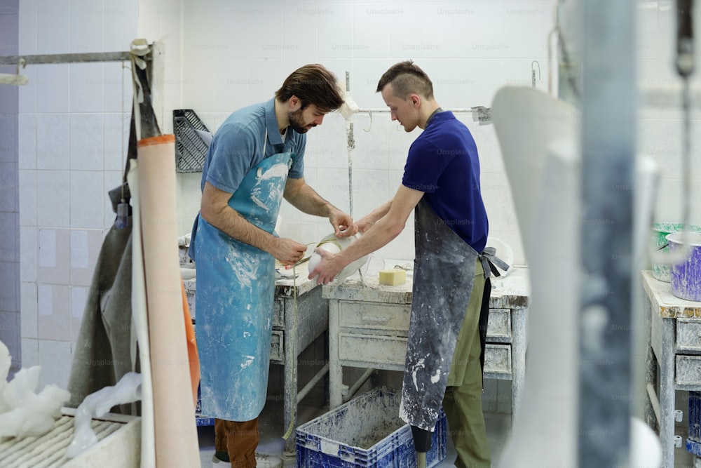 Jeune homme handicapé en tablier aidant son collègue à mesurer le diamètre du plâtre pendant le travail dans une usine de prothèses