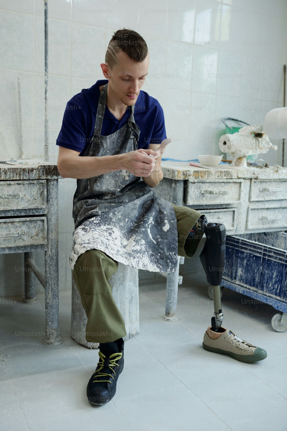 Young restful man with disability sitting by small table in workshop of contemporary prosthetic factory during break