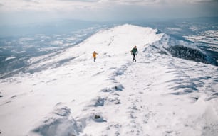 Two hikers ascending over snowy mountain ridge.