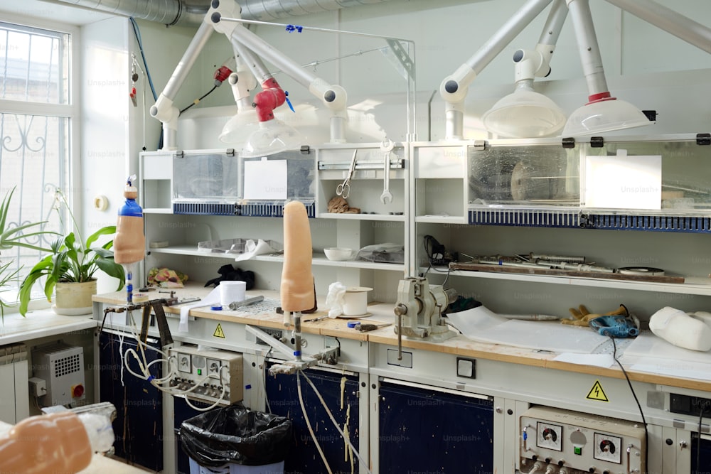Posto di lavoro di operaio contemporaneo di manifattura protesica dotato di banchi da lavoro, lampade e attrezzature per la produzione di prese
