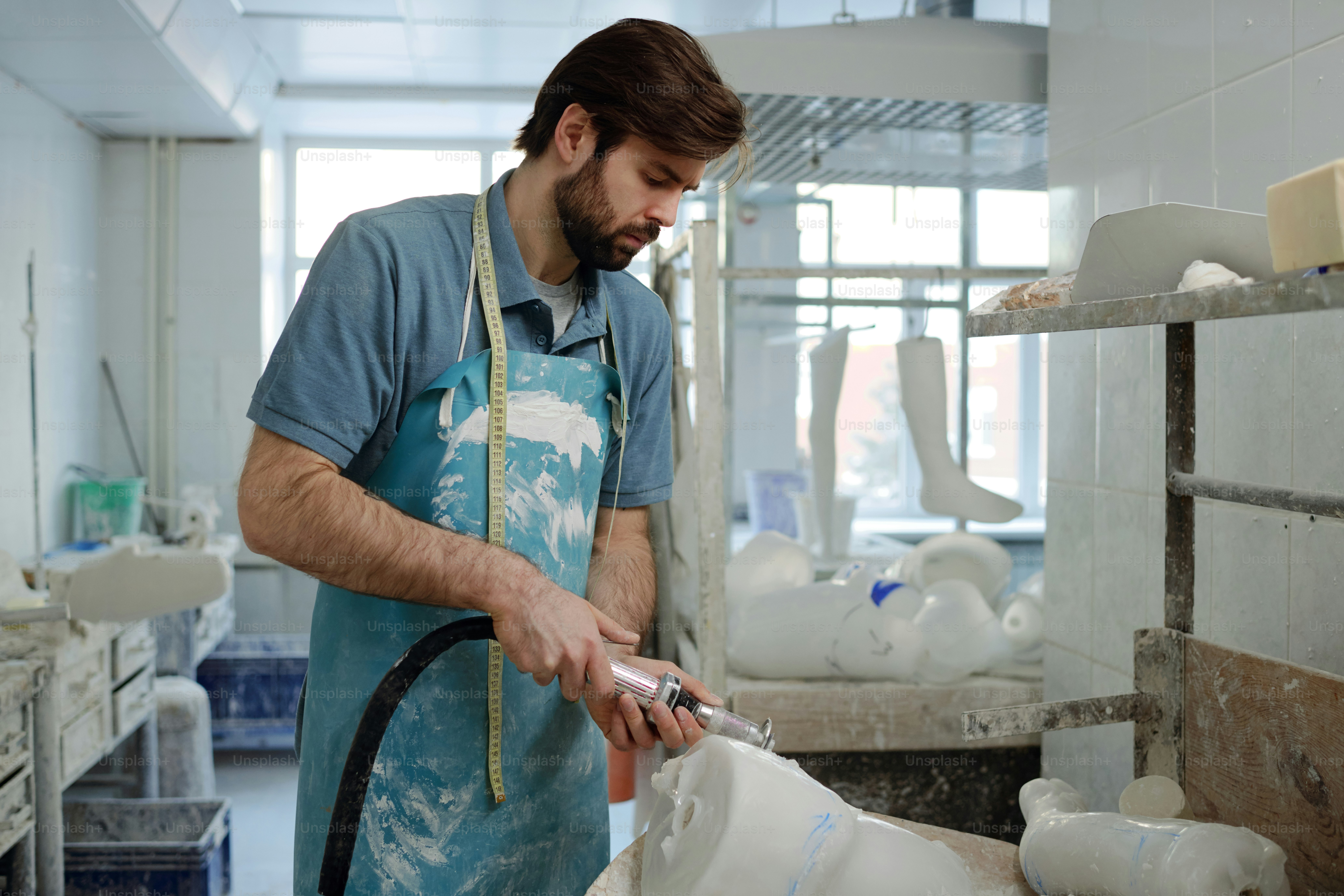 Side view of bearded skilled worker od prosthetic factory with electric worktool cutting upper part of leg plaster cast by workbench