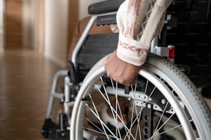 Close-up of man with disability rotating wheels of wheelchair while moving forwards along corridor of his apartment