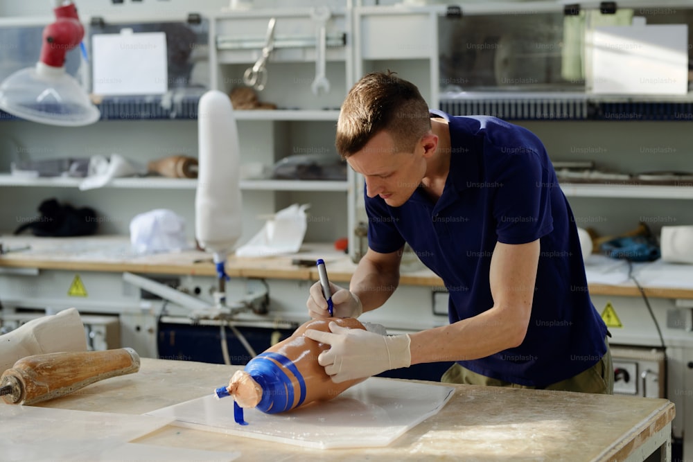 Arbeiter der Manufaktur mit blauem Textmarker, der sich über die Werkbank beugt, während er Markierungen auf Silikonfolie der Beinprothese legt