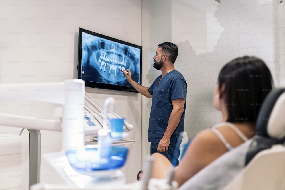 Stock photo of male worker of dental clinic showing an x-ray to a patient.