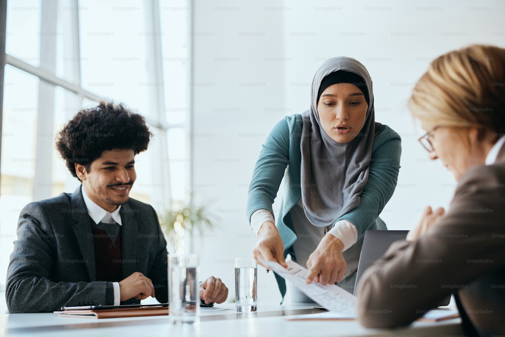 Multiracial group of business people cooperating while going through paperwork on a meeting at corporate office. Focus is on Muslim businesswoman.