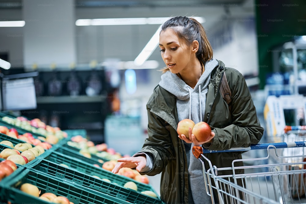 Young woman choosing apples while buying in grocery store.